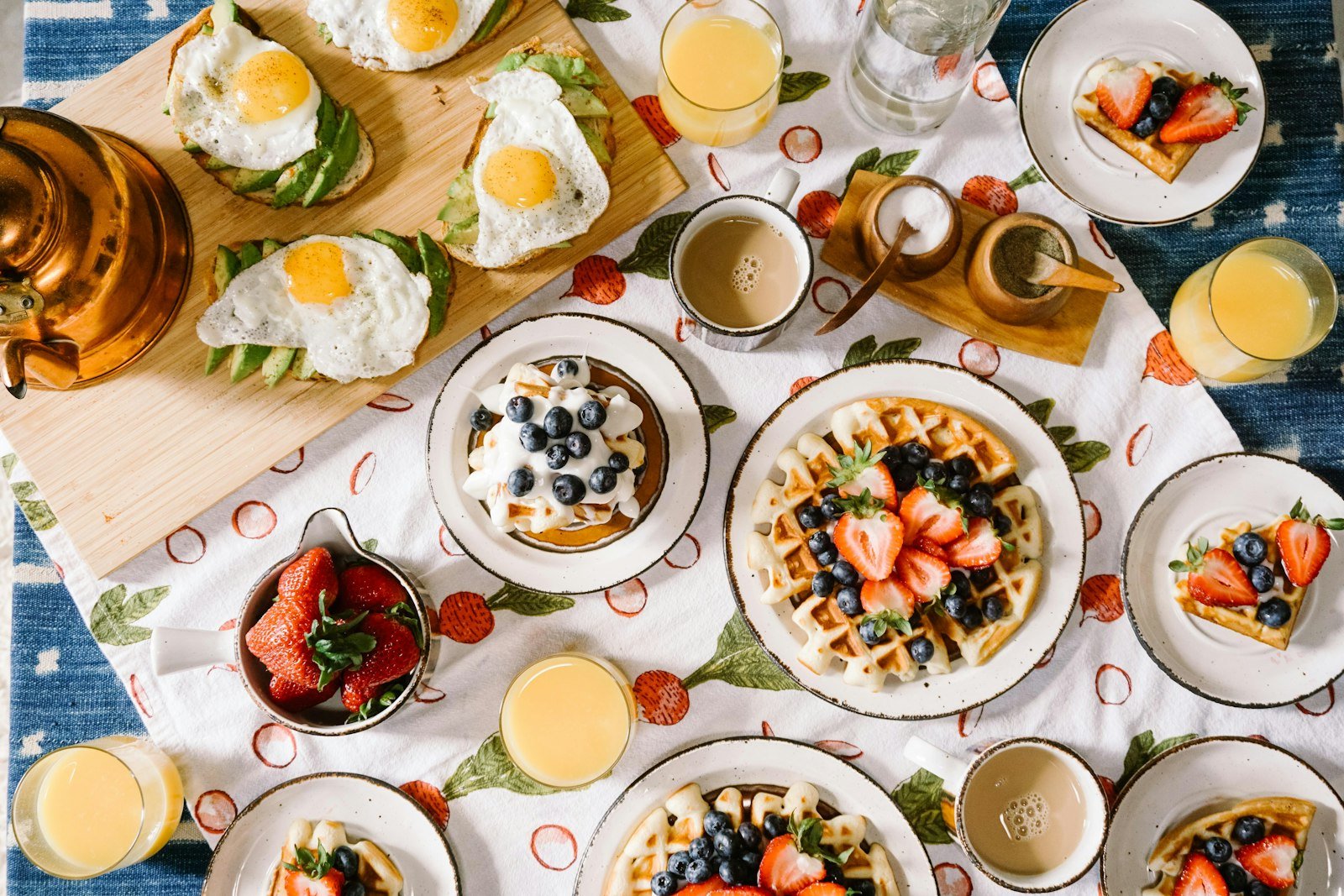 An overhead spread of a fresh brunch — eggs, avocado, coffee and waffles.